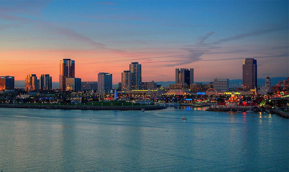 The Long Beach, California skyline at dusk — downtown towers reflected in the harbor, with a warm pink and blue twilight sky.